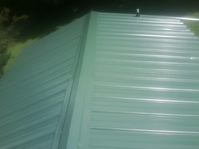 New green metal panels meeting at the ridge of a roof — Flat Roof Repair work by our crew in Irwin